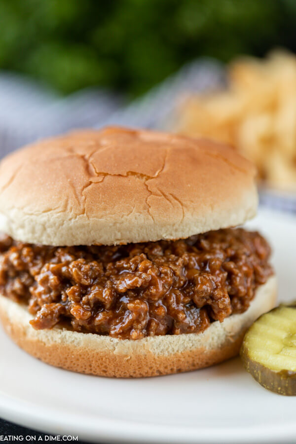 Close up image a sloppy joes on a bun with pickles on the side. 