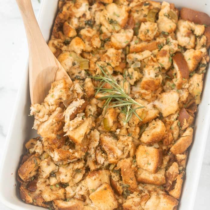 Close up image of stuffing in baking dish with a serving on a wooden spoon. 