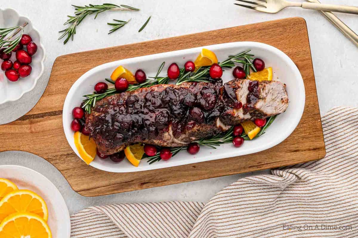 Close up image of cranberry pork tenderloin on a platter with fresh slice oranges and cranberries
