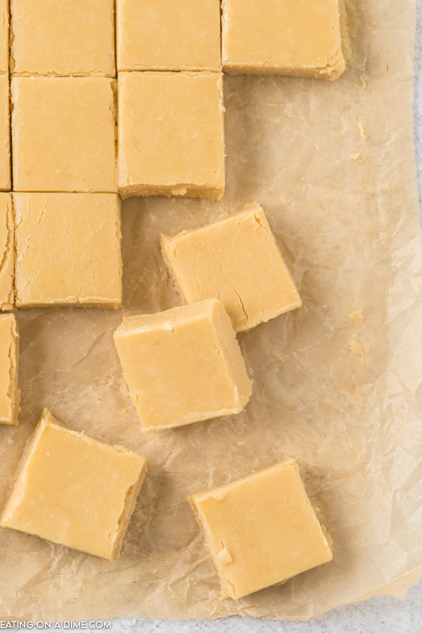 Caramel Fudge cut into small pieces on a piece of parchment paper and some of the pieces are stacked on top of each other. 