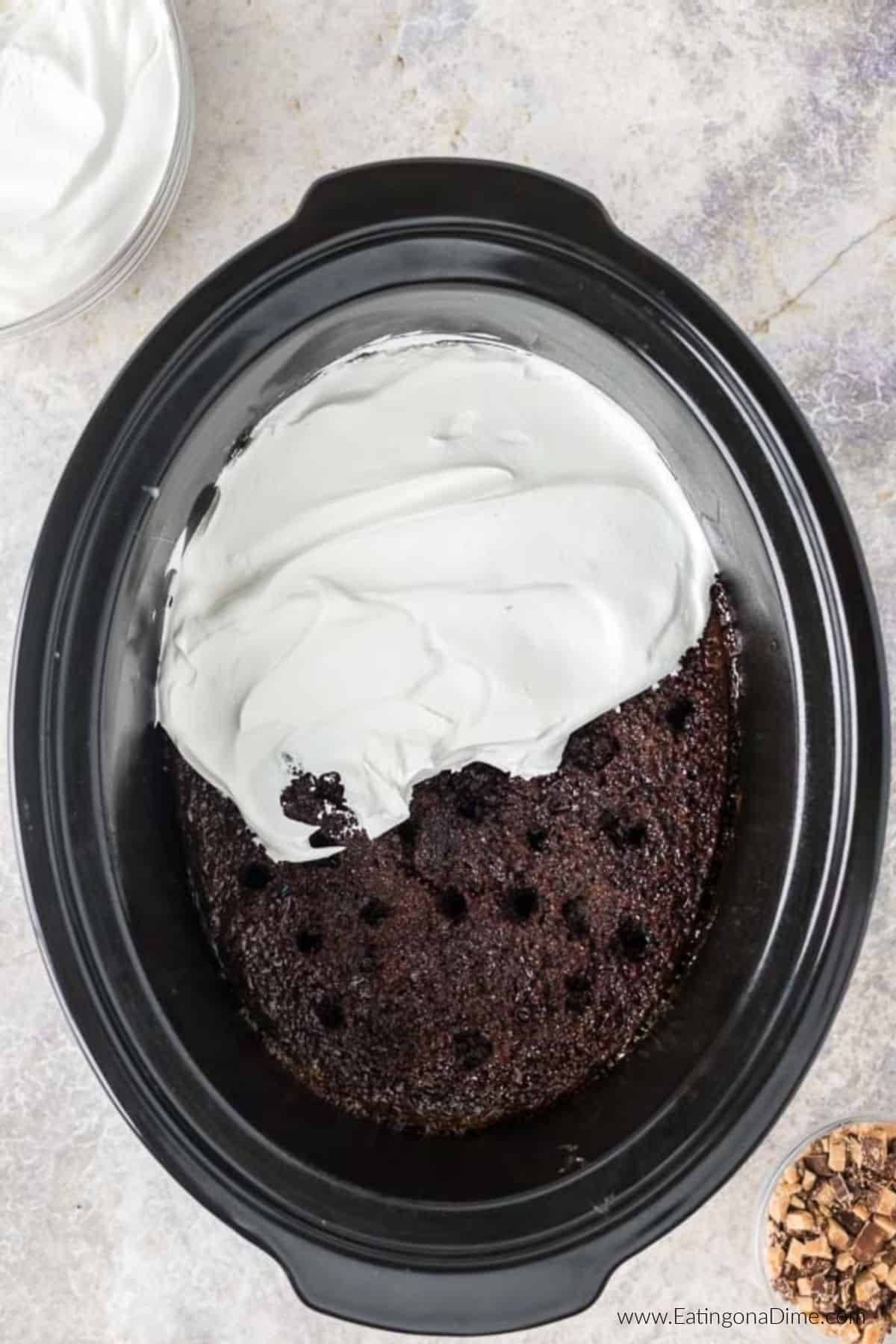 Spreading whipped cream over the cake in the crockpot.