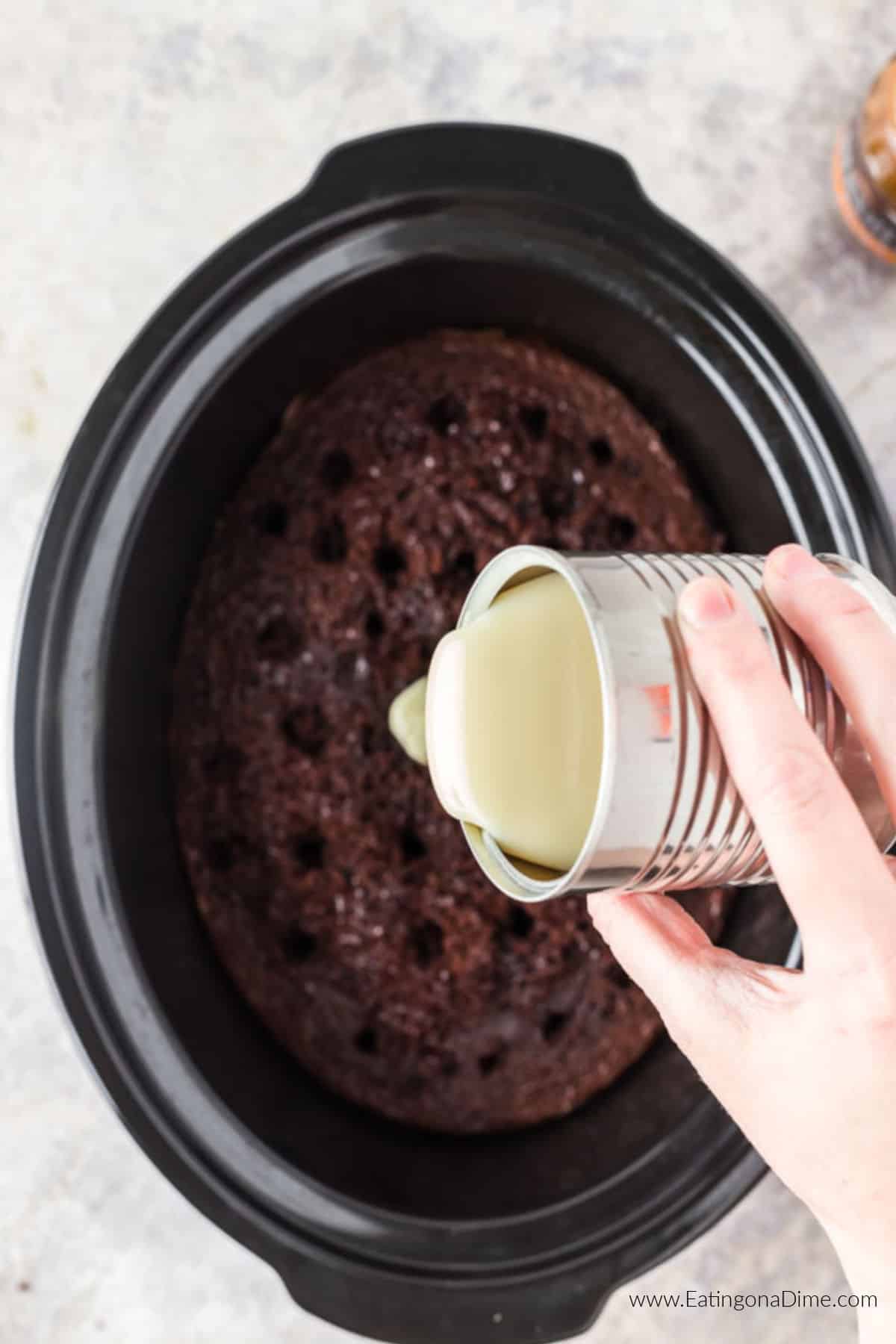 Pouring sweetened condensed milk over the cake in the crockpot.