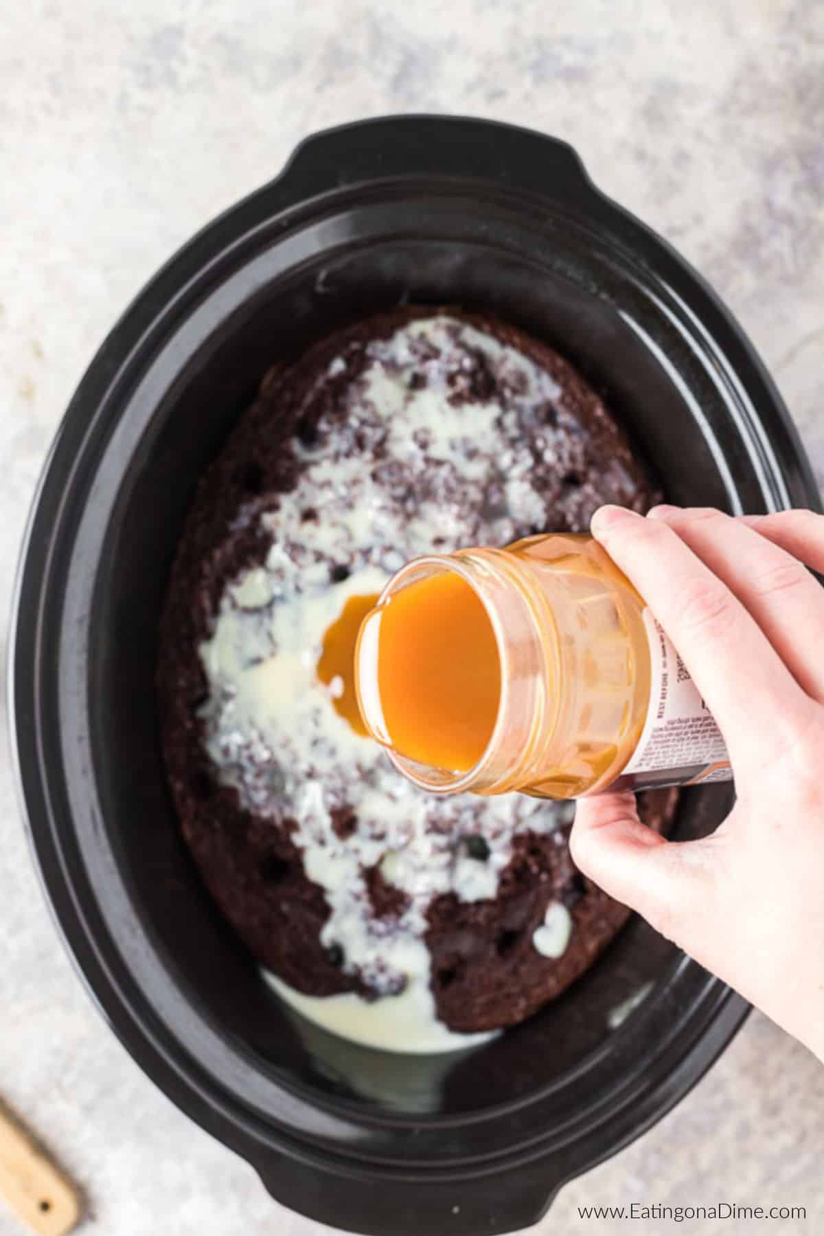 Pouring caramel sauce over the sweetened condensed milk and cake in the crockpot.