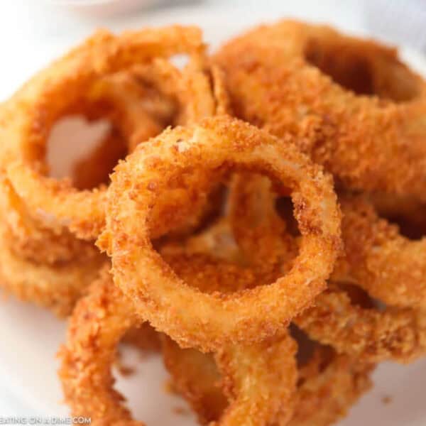 A close-up of a plate piled with crispy, golden-brown fried onion rings, each coated in a crunchy breading.