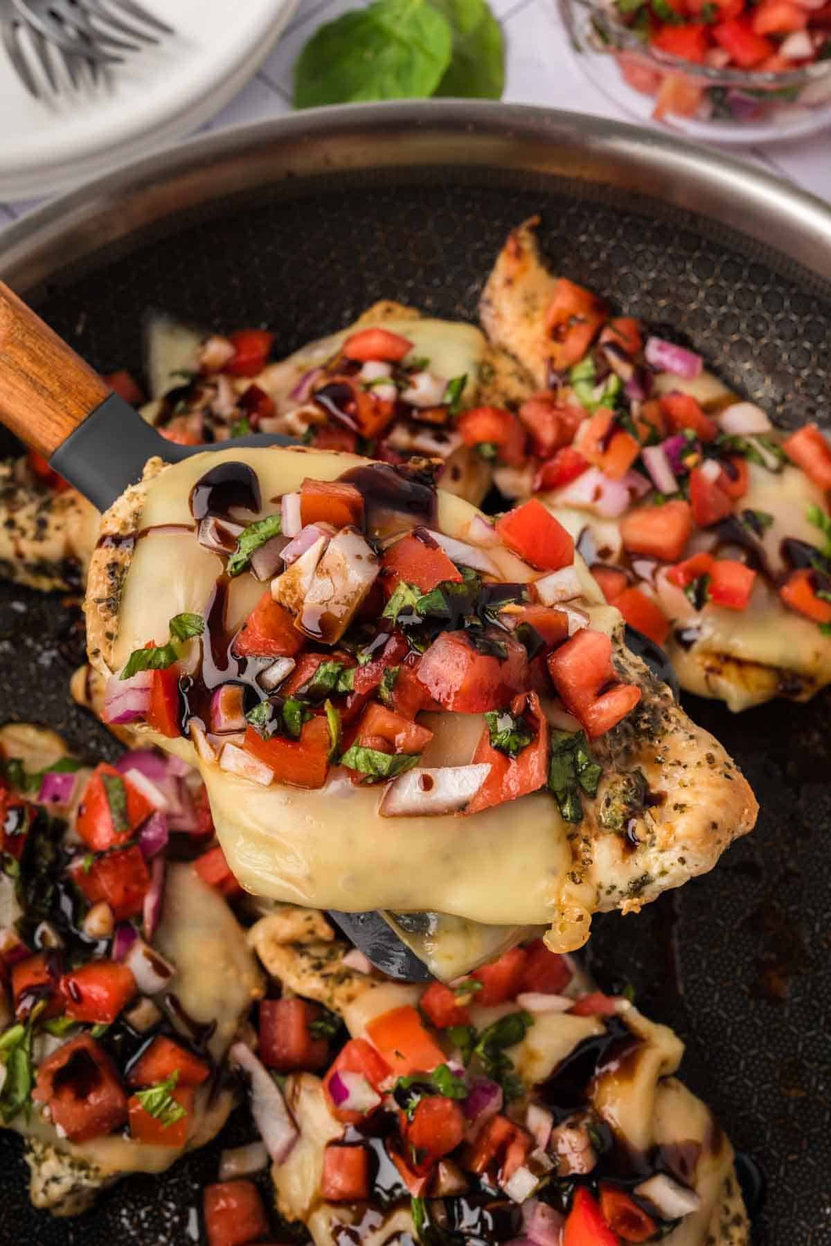 Chicken Bruschetta in a skillet with a serving on a spatula
