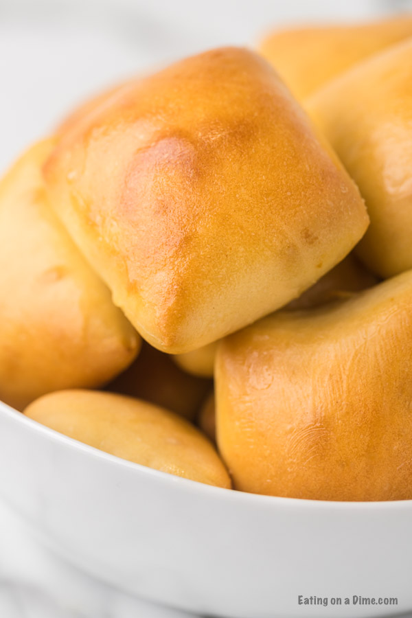 White serving bowl of rolls piled high. 