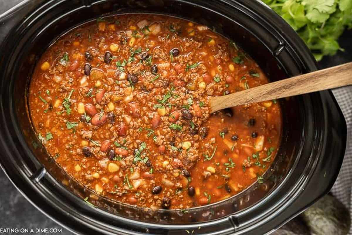 Taco chili cooked in a crock pot topped with fresh diced cilantro with a serving spoon in the taco chili.  