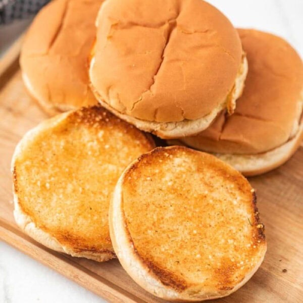 Stacked hamburger buns on a cutting board.