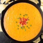 A skillet filled with creamy orange velveeta chili cheese dip, garnished with chopped tomatoes and green onions, surrounded by tortilla chips.