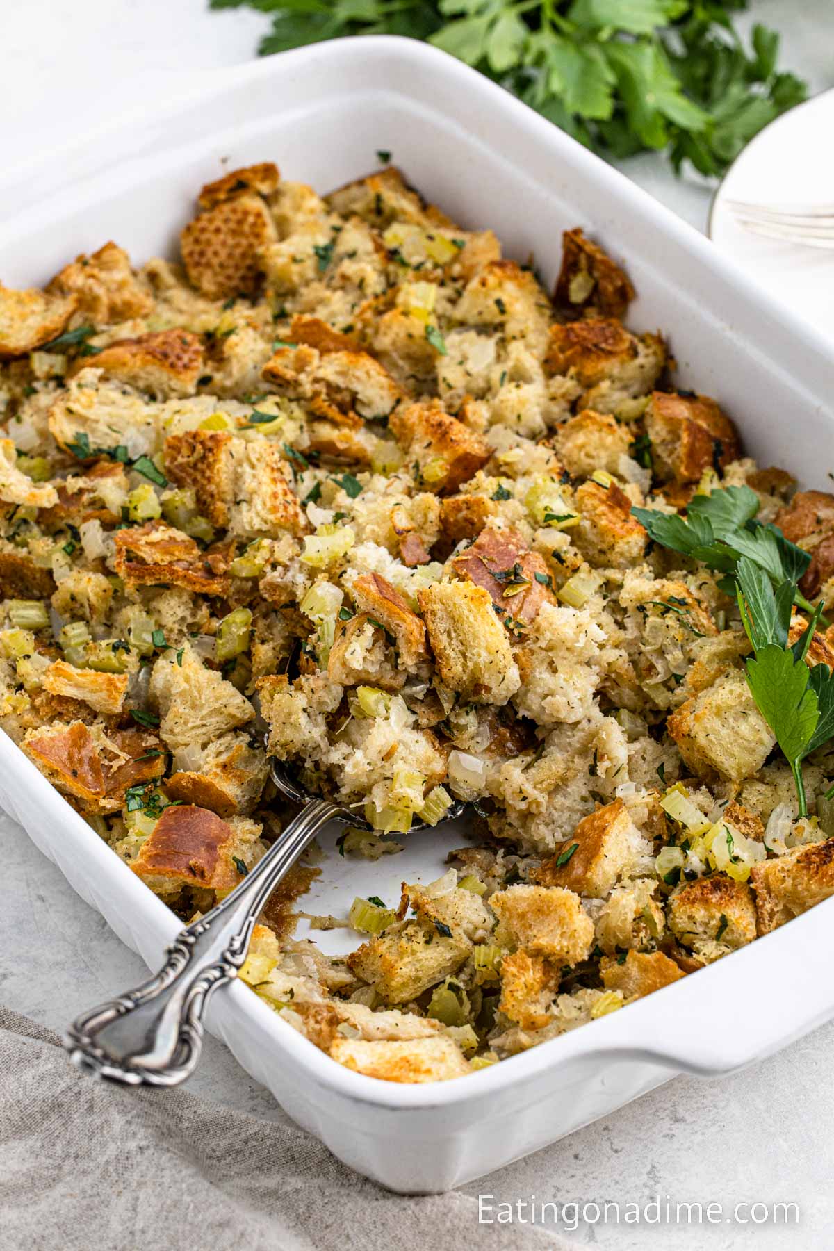 Close up image of stuffing in baking dish with a serving on a large silver serving spoon.  