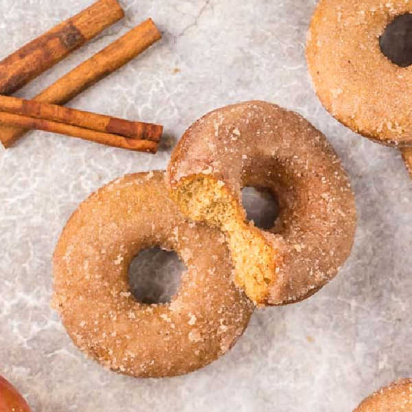 2 donuts stacked on top of each other with a bite taken out of the top donut. 