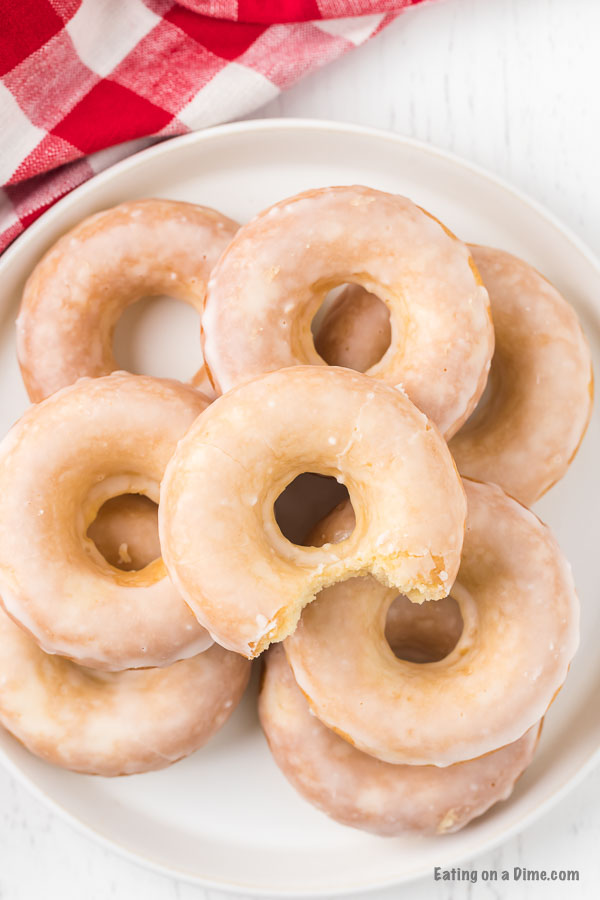 Close up image of glazed donuts stacked on a white plate. 