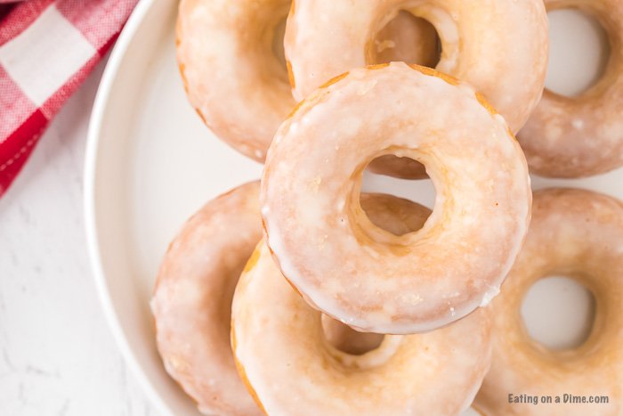 Close up image of glazed donuts on a white plate stacked. 