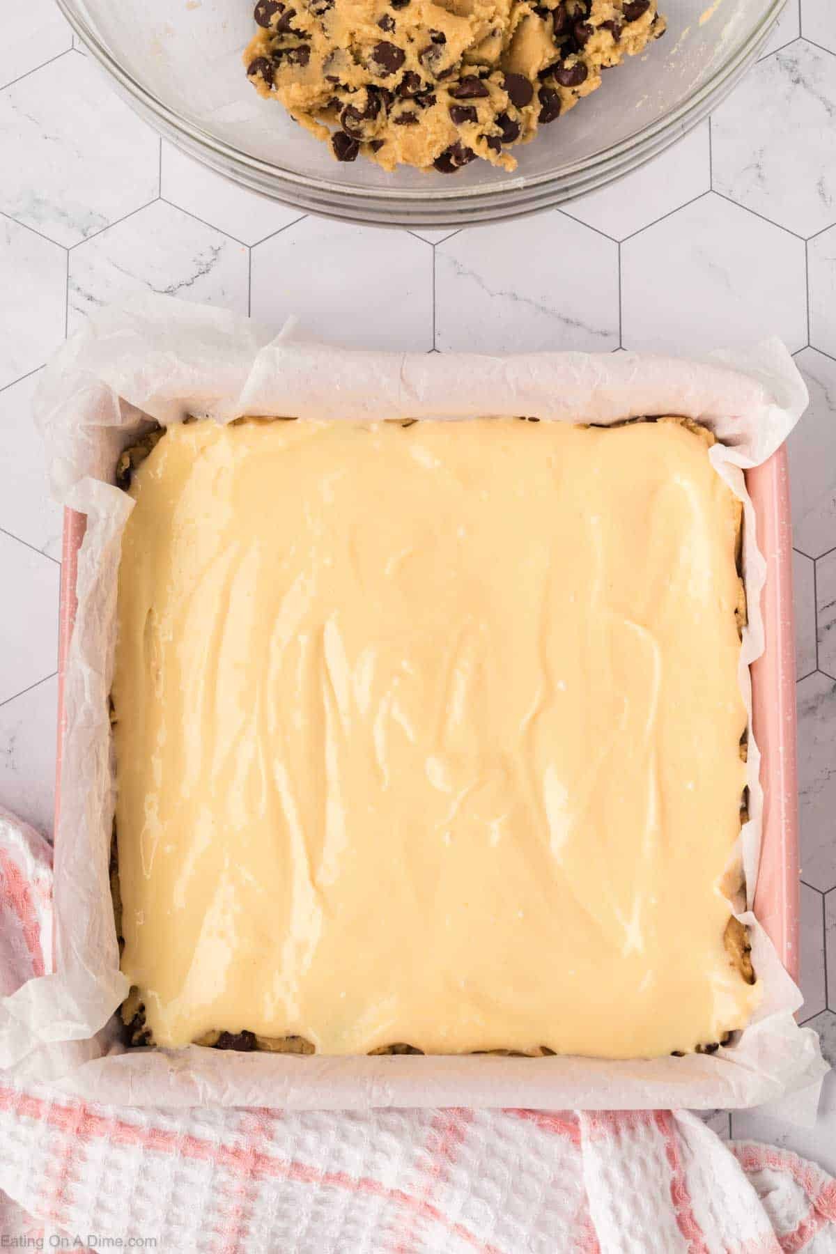 Cream cheese mixture spread over the chocolate chip cookie dough in a square pan lined with parchment paper