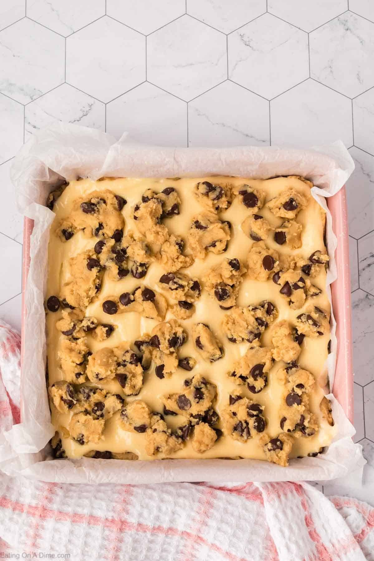 Chocolate Chip cookie dough crumbled over the top of the cheesecake mixture in a baking dish lined with parchment paper