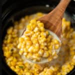 Corn in the slow cooker with a serving on a wooden spoon.