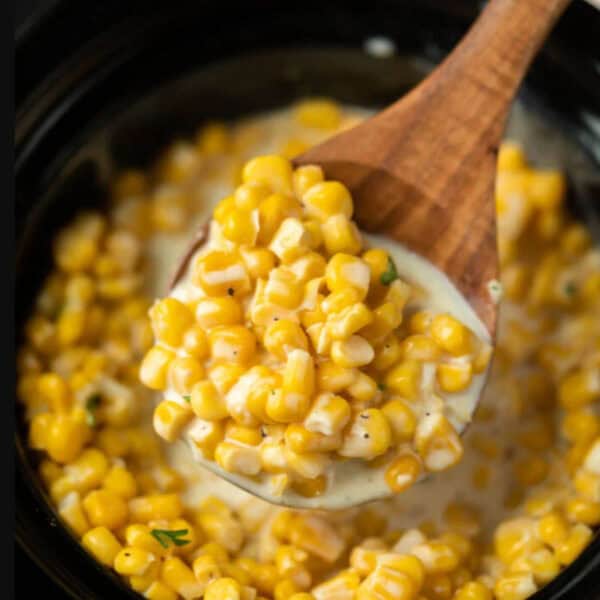 Corn in the slow cooker with a serving on a wooden spoon.