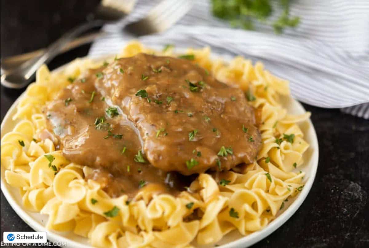 cube steak served over egg noodles on a white plate