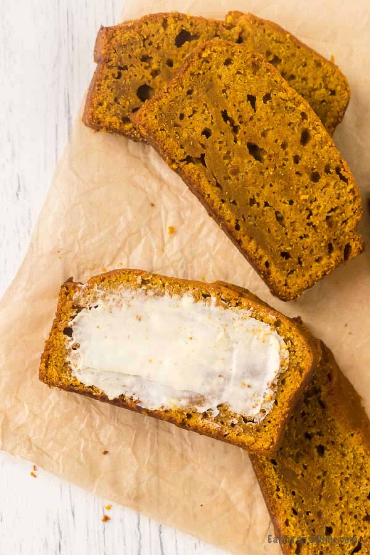 This is the BEST pumpkin bread recipe. It is easy to make and this Pumpkin Bread Recipe tastes amazing! Try this recipe for Pumpkin Bread. Slices of pumpkin bread, crafted from a beloved recipe, rest on parchment paper with one slice generously spread with butter.