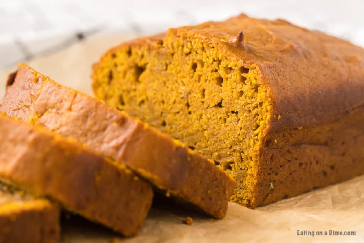 This is the BEST pumpkin bread recipe. It is easy to make and this Pumpkin Bread Recipe tastes amazing! Try this recipe for Pumpkin Bread. Pumpkin bread being sliced on parchment paper.
