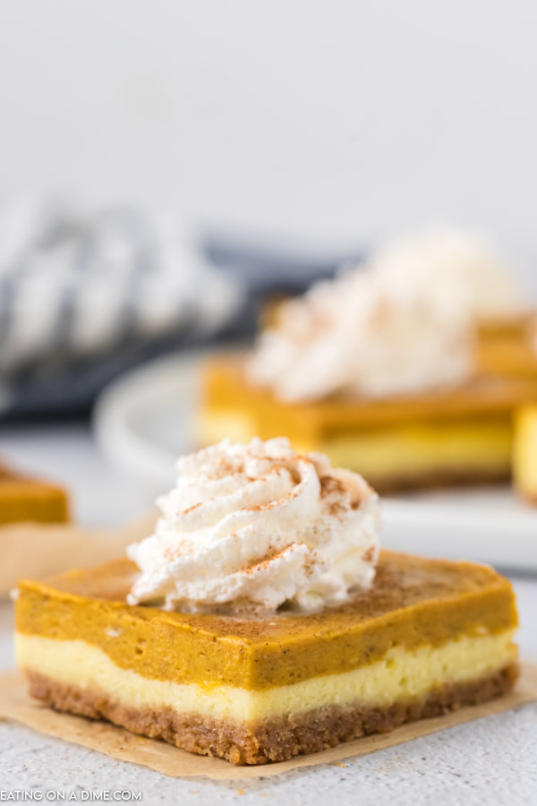 Close up image of a square piece of pumpkin cheesecake bars with whipped topping. 