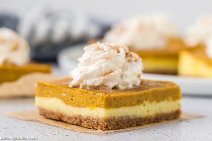 Close up image of a square piece of pumpkin cheesecake bars with whipped topping. 