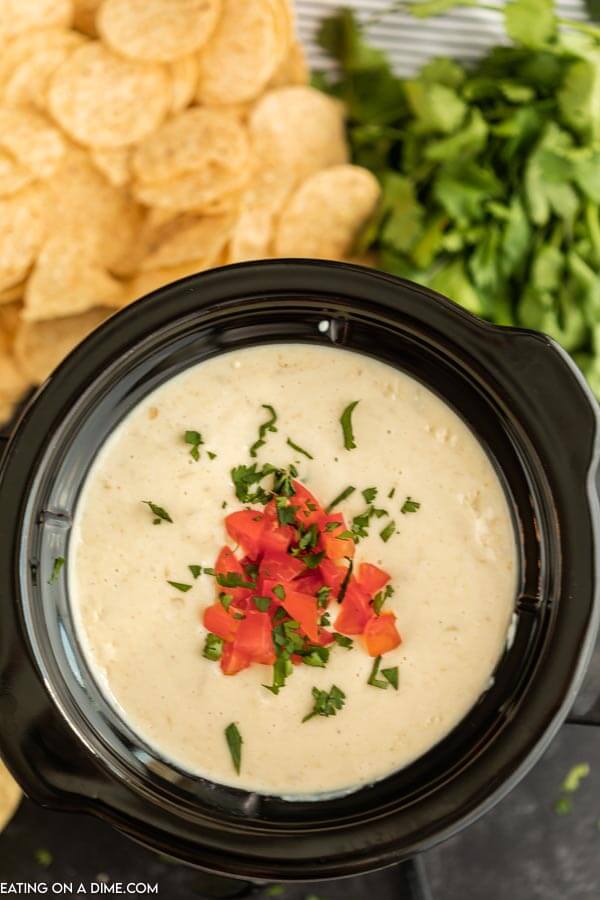 White cheese dip in a small black crock pot topped with diced tomatoes and chopped cilantro 