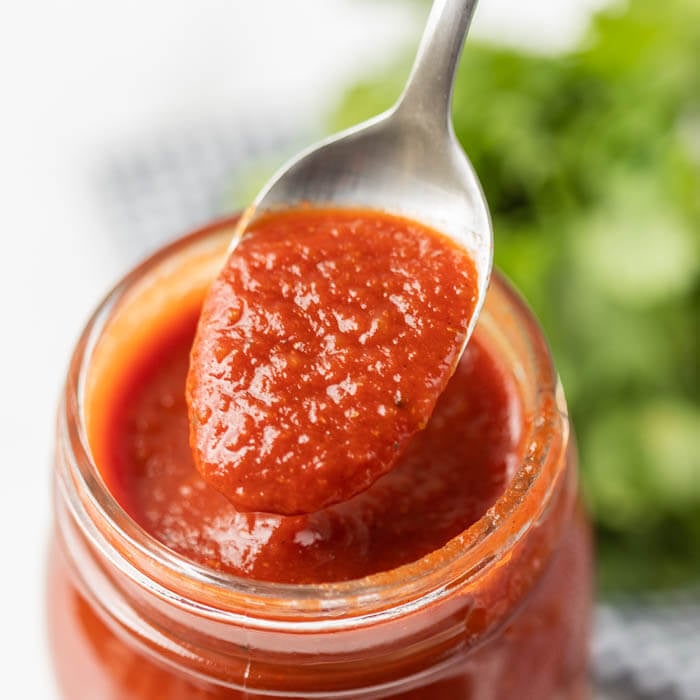 Close up image of a red enchilada sauce in a mason jar on a spoon. 