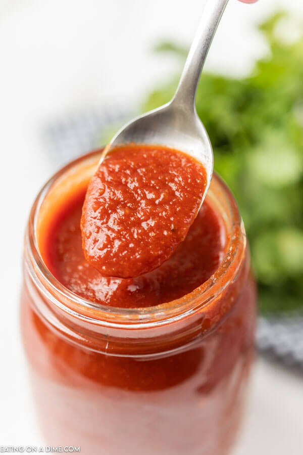 Close up image of red enchilada sauce in a mason jar on spoon. 