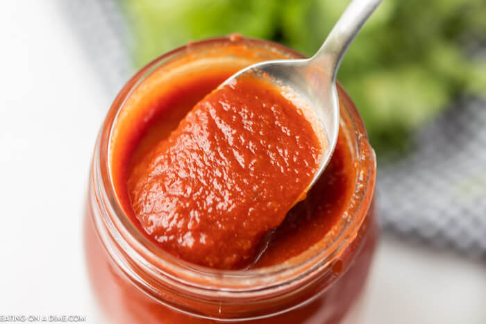 Close up image of red enchilada sauce in a mason jar with a serving on a spoon. 
