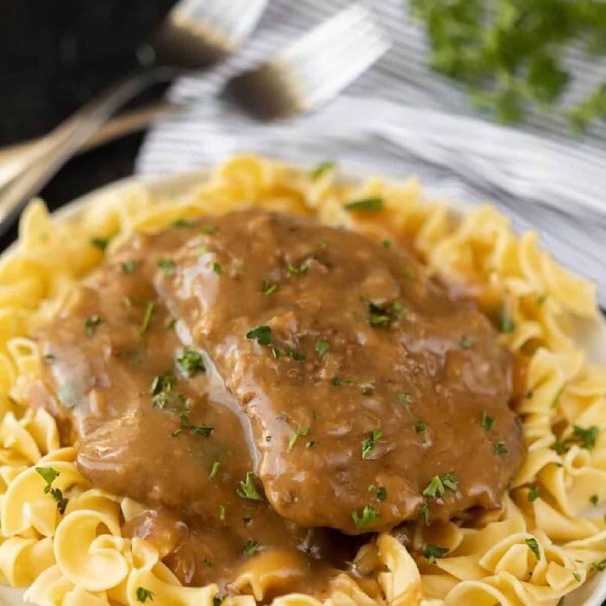 Cube steak over noodles with gravy on top on a white plate.