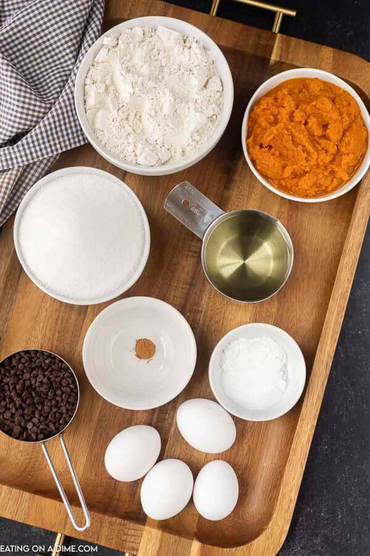 The ingredients needed to make pumpkin chocolate chip bars: flour, sugar, baking powder, baking soda, pumkin pie spice, eggs, canned pumpkin, oil and mini chocolate chips 