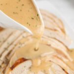 A close up of the gravy being poured over the turkey.