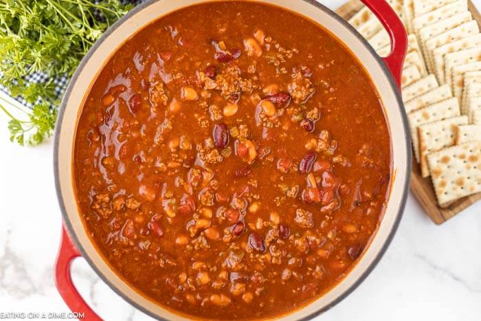 Close up image of chili in a red dutch oven with a side of saltine crackers. 