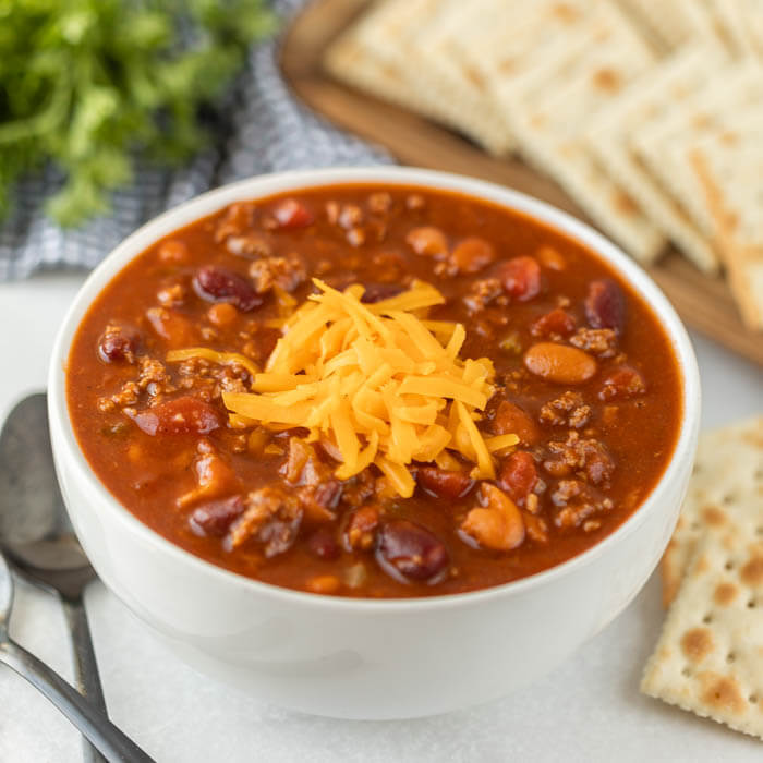 Close up image of Wendy's chili in a white bowl with two spoons and crackers. 