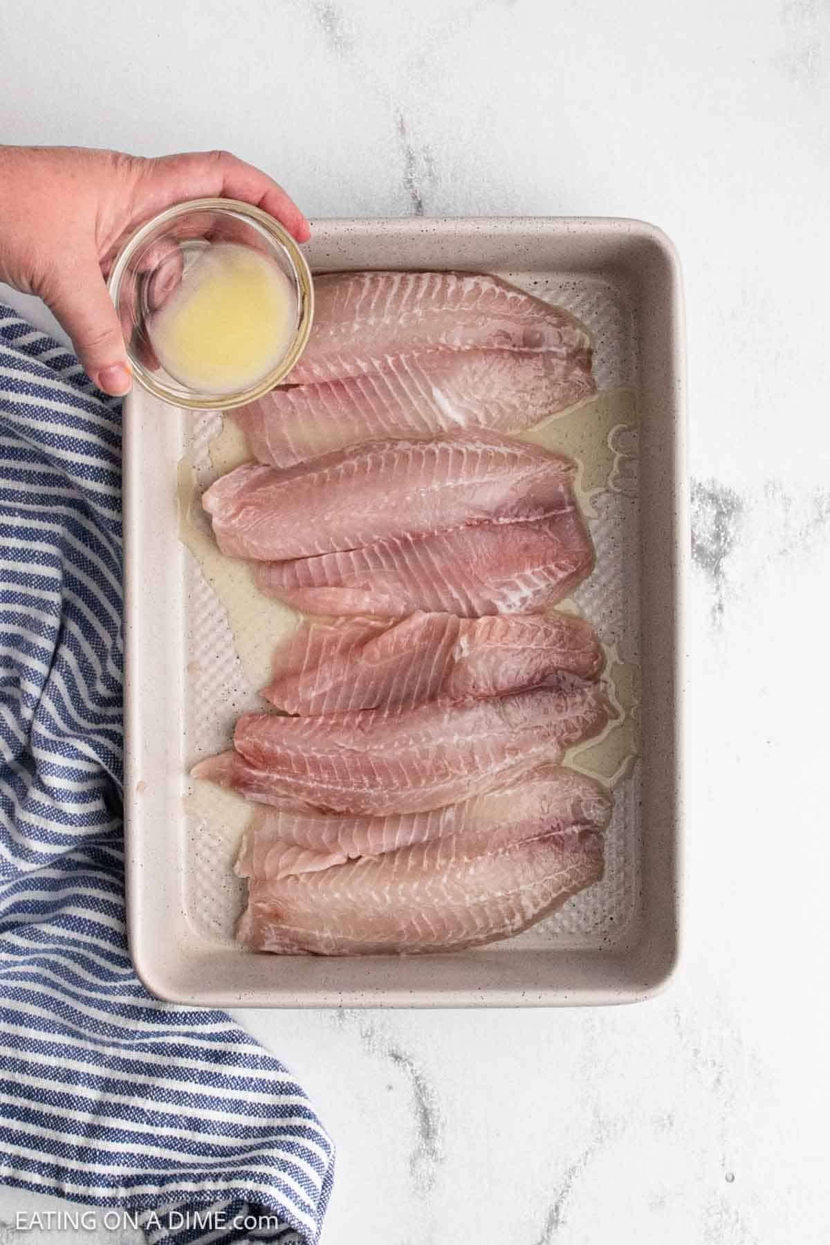 Lemon being poured over the fish in the baking dish.