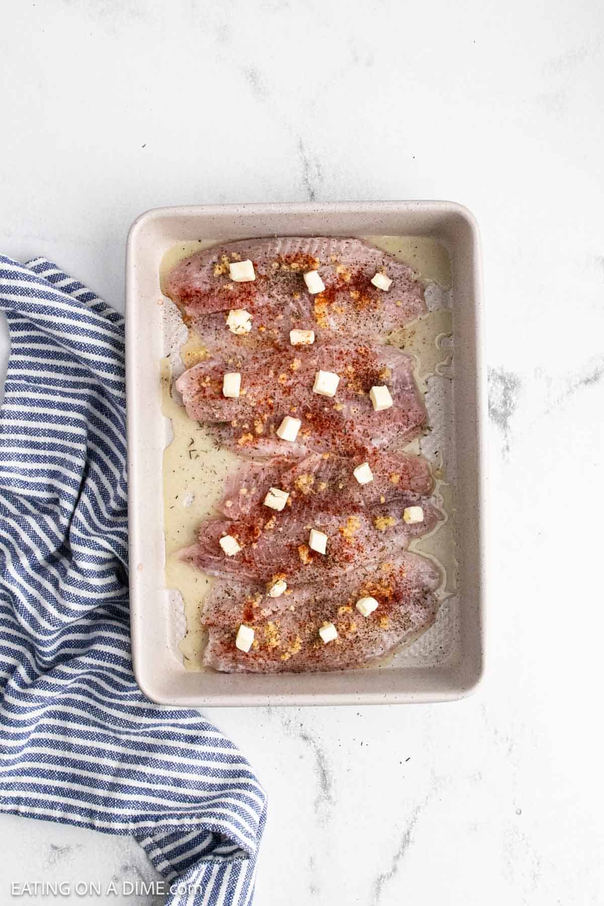 Seasoning, garlic, and butter topped the fish in the baking dish.