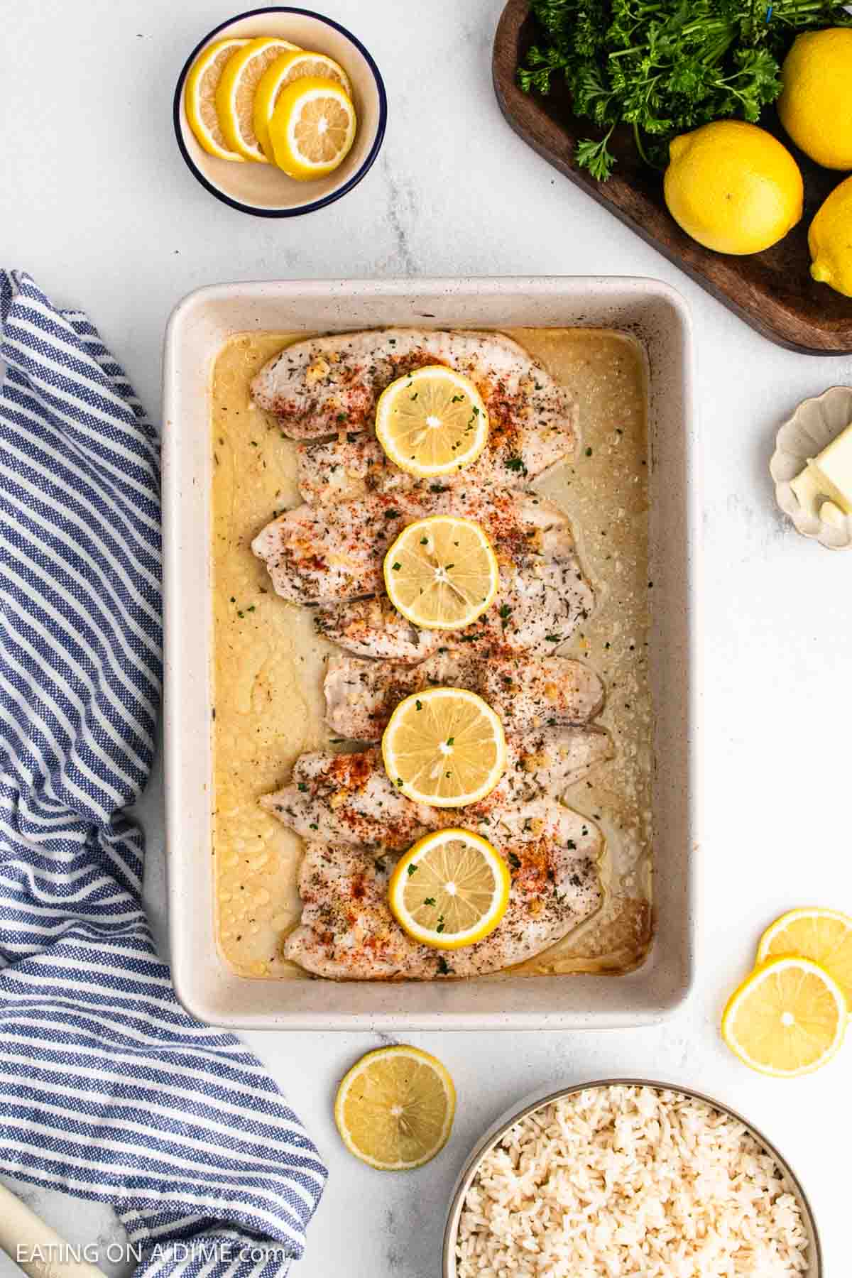 Baked fish in a baking dish topped with lemon slices.