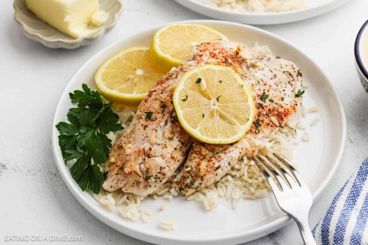 Baked tilapia on a plate over rice and topped with slices of lemon.