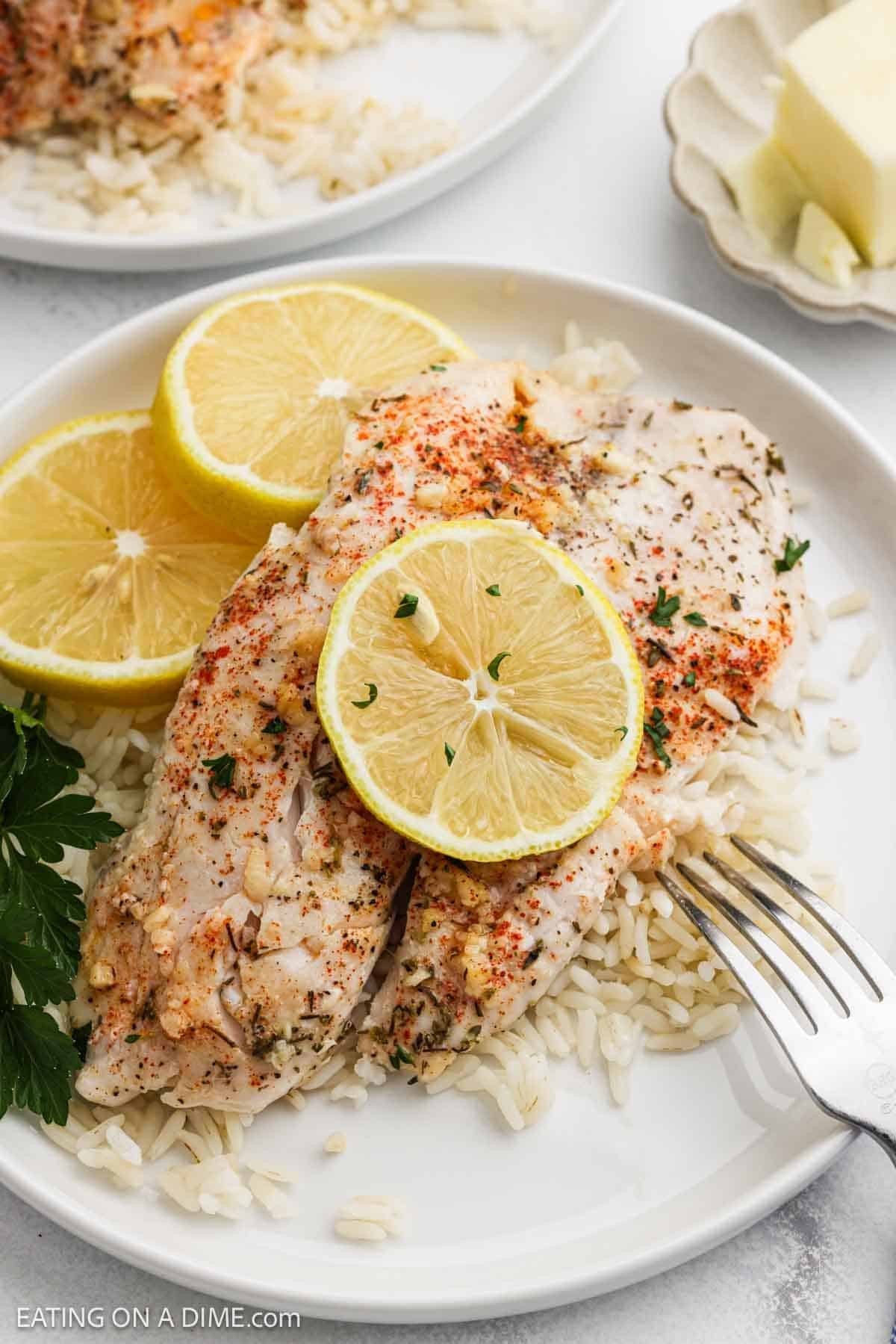 Baked fish over rice on a plate topped with lemon slices.