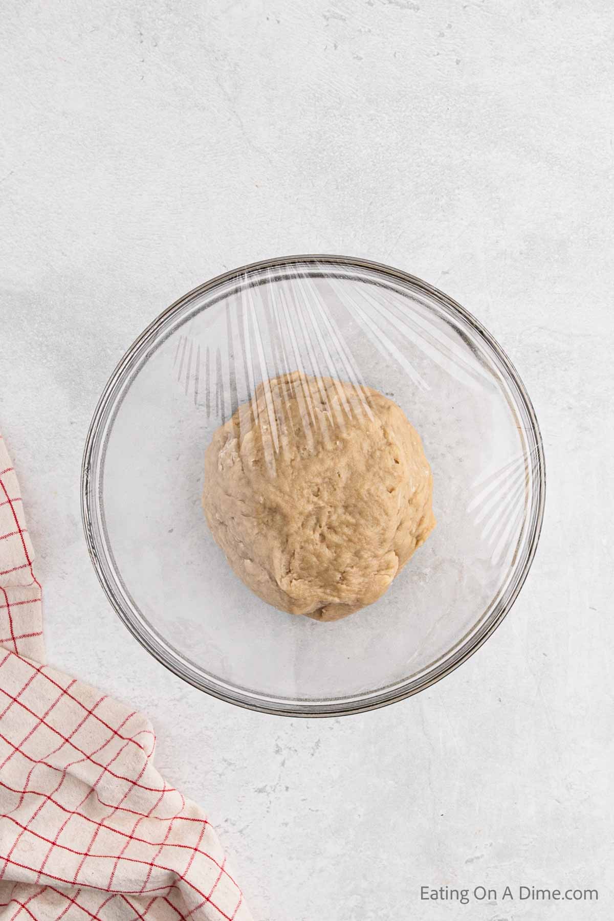 Dough ball in a bowl covered with plastic wrap