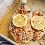 Baked tilapia in a baking dish topped with slices of lemon.