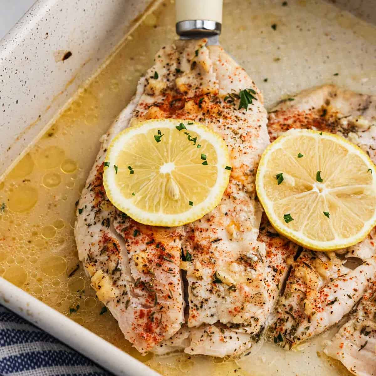 Baked tilapia in a baking dish topped with slices of lemon.