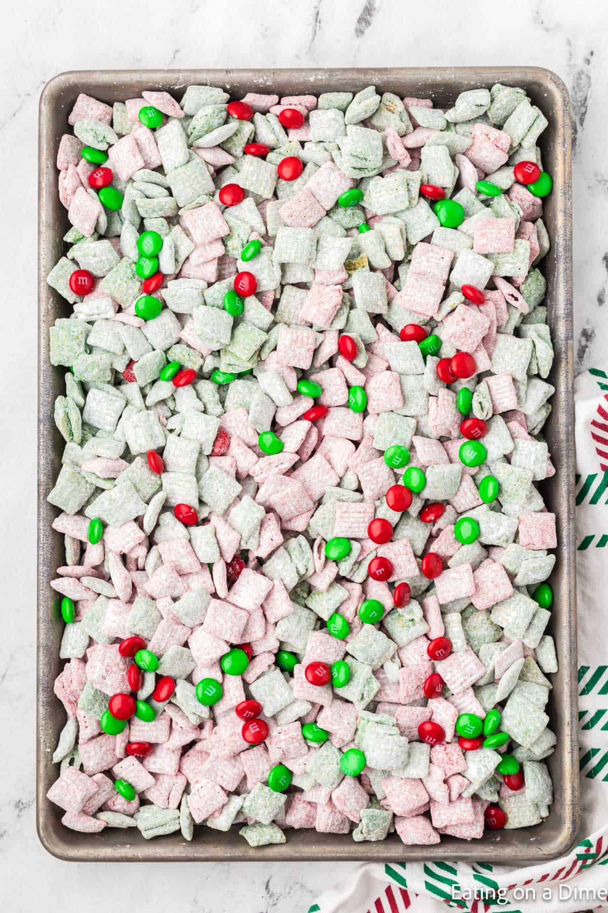 Christmas Puppy Chow on a baking sheet topped with Red & Green M&M's. 