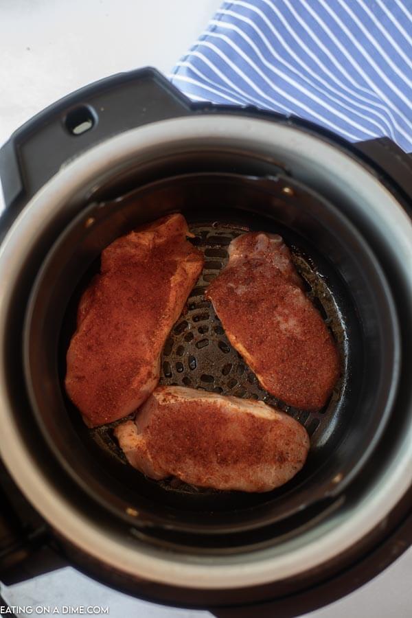 Close up image of uncooked pork chops in an air fryer. 