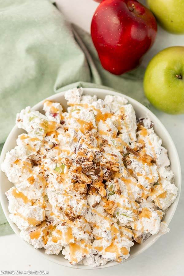 Close up image of snicker apple salad in a white bowl drizzled with caramel sauce. 