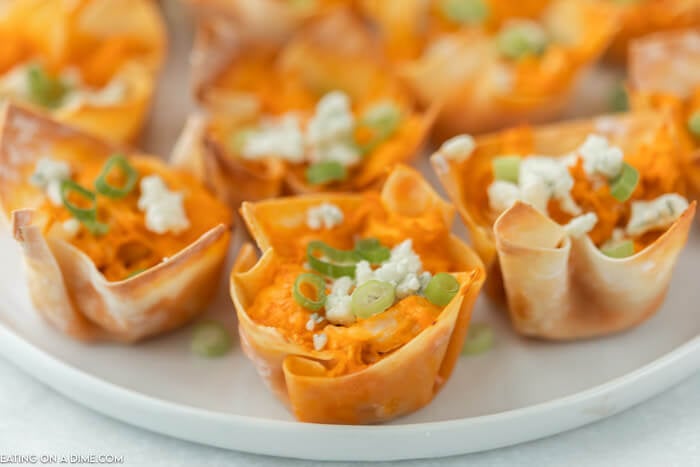 Close up of buffalo chicken wonton cups topped with blue cheese and diced green onions on a white plate 