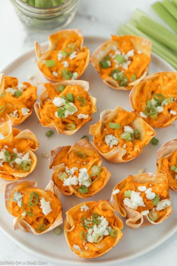 Overview of buffalo chicken wonton cups topped with blue cheese and diced green onions on a white plate 