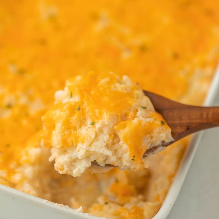 A close up of a wooden spoon scooping out a serving of these cheesy potatoes from the casserole. 