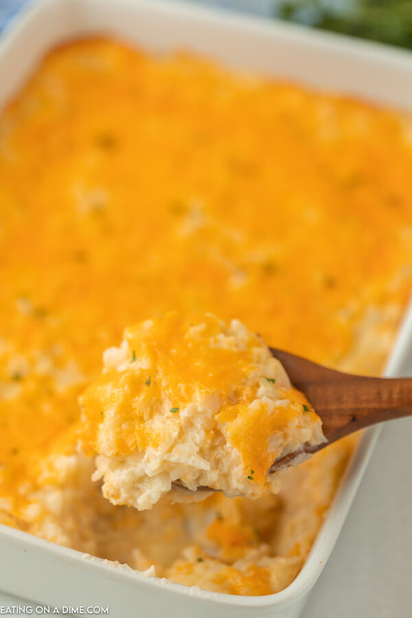 A wooden spoon scooping out a serving of these cheesy potatoes from the casserole. 
